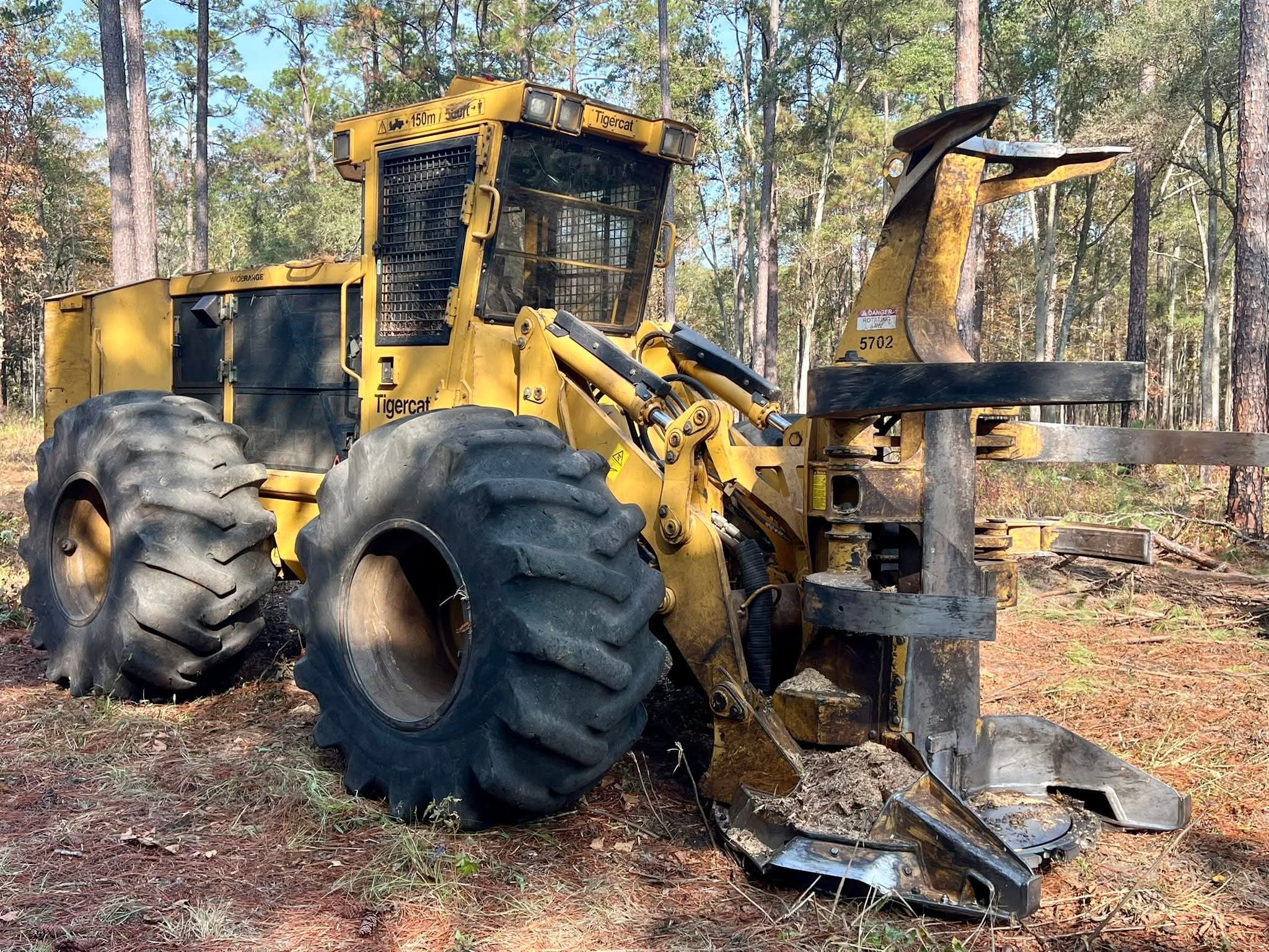 Yellow Tigercat feller buncher heavy machinery situated on freshly cleared ground within a wooded area, showcasing professional land clearing services.
